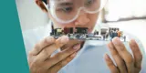 A man wearing safety glasses and examining the inside of a small device